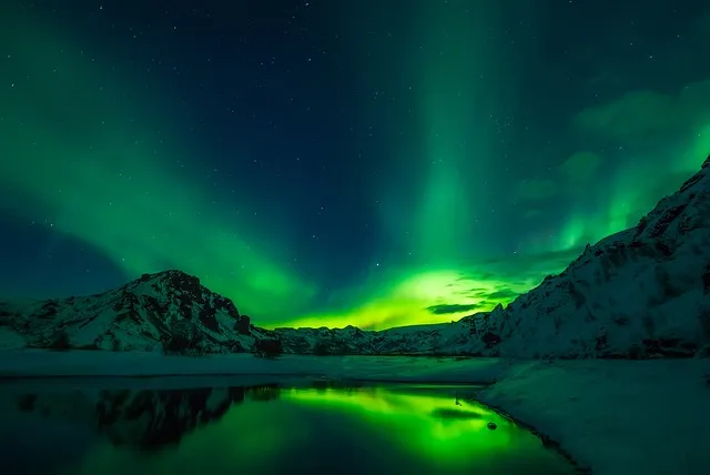 Aurora borealis dancing over a snowy Icelandic landscape with mountains