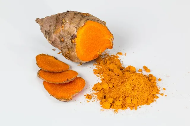 Golden turmeric powder and fresh root on a wooden table
